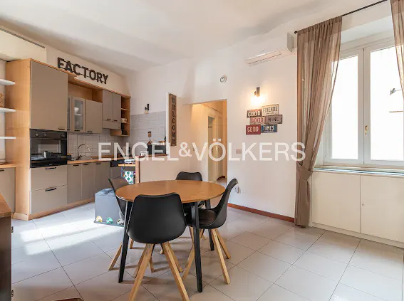 Modern kitchen and dining area with light wood cabinets, a round wooden table, four black chairs, and tile flooring.