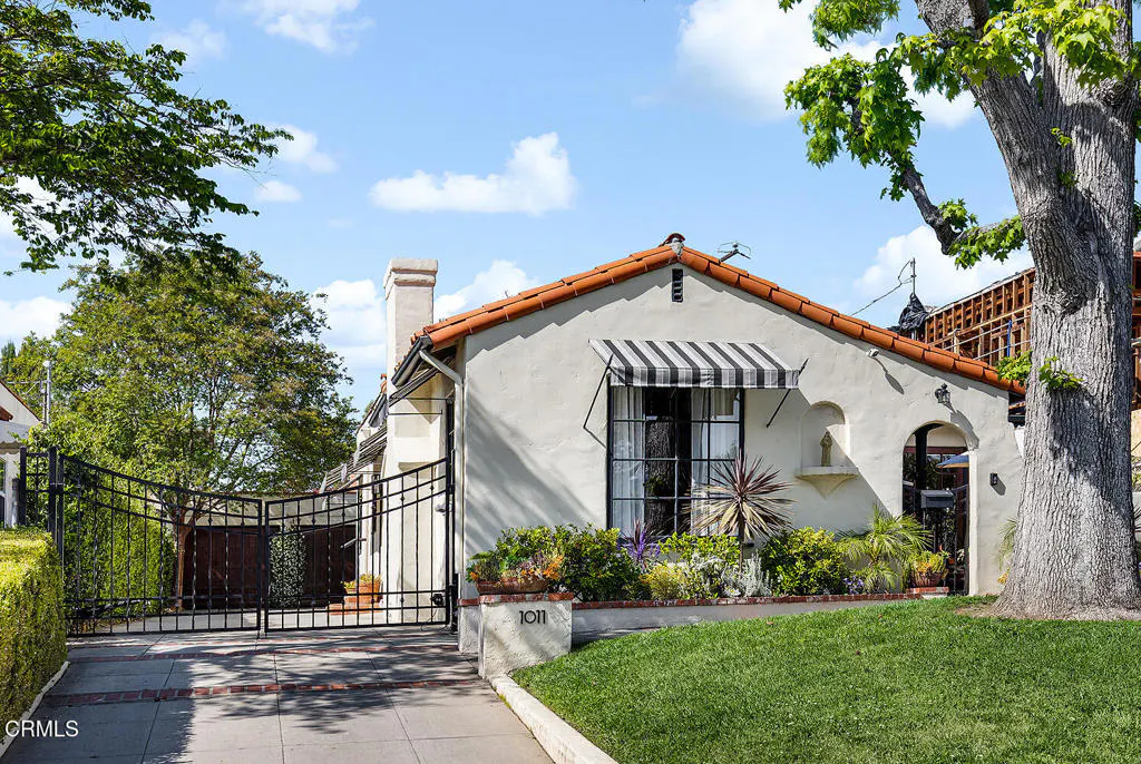 Exterior of a white stucco house with a red tile roof, black and white striped awning, and black iron gate.