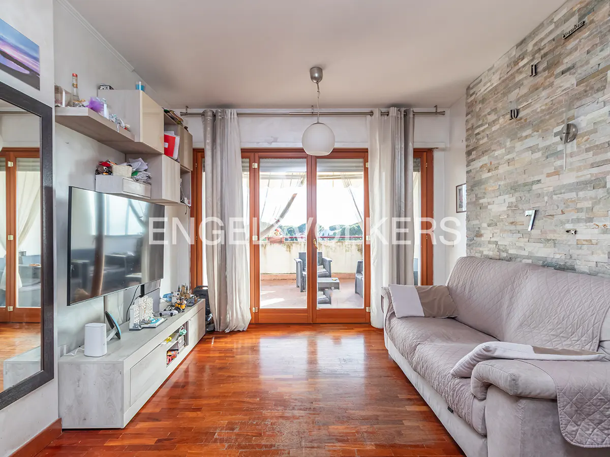 Living room with wood floors, a gray sofa, and a TV. Balcony doors lead to an outdoor seating area.