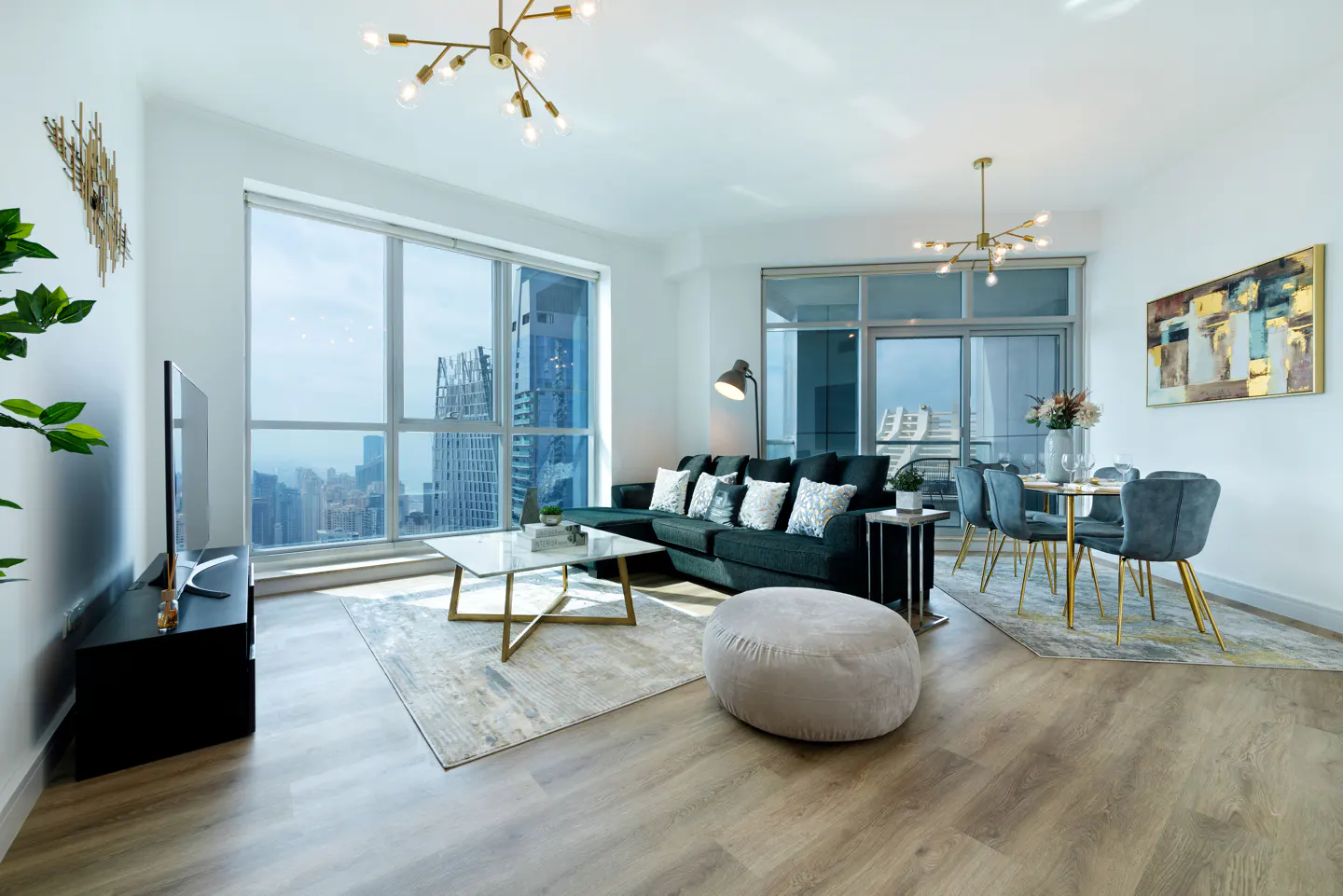 Bright, modern apartment interior with a dark green sofa, dining table, and city views through large windows.