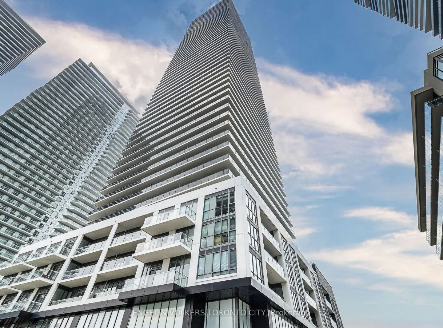 Low angle view of a tall, modern condo building with balconies against a blue sky with clouds.