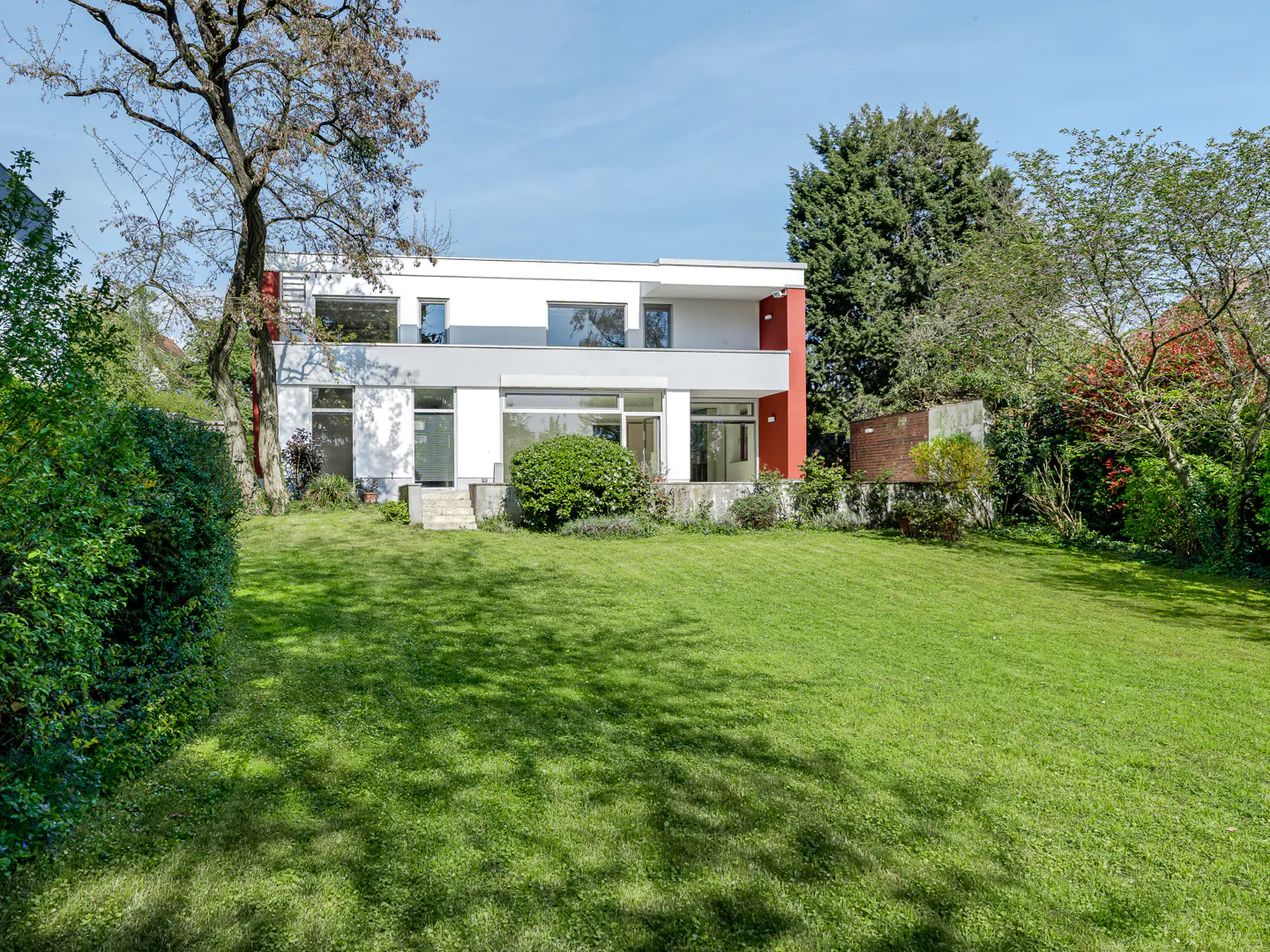 Two-story modern house with white and gray exterior, red accent wall, and large green lawn.