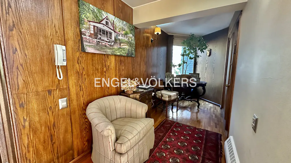 A real estate photo shows a foyer with wood paneling, a striped armchair, and a red patterned rug.