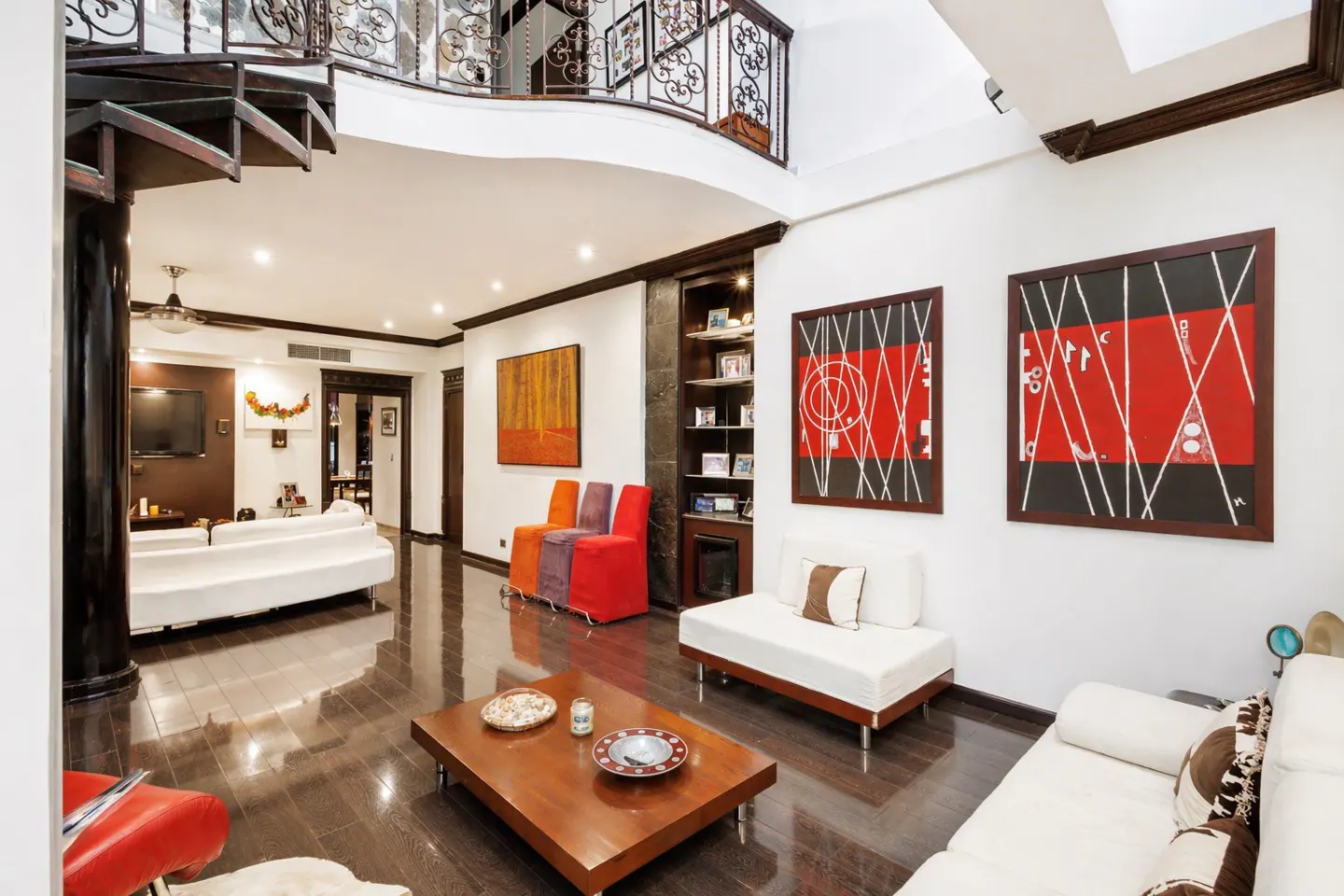 A living room with white sofas, a wooden coffee table, and abstract art on the walls. A spiral staircase is visible in the background.