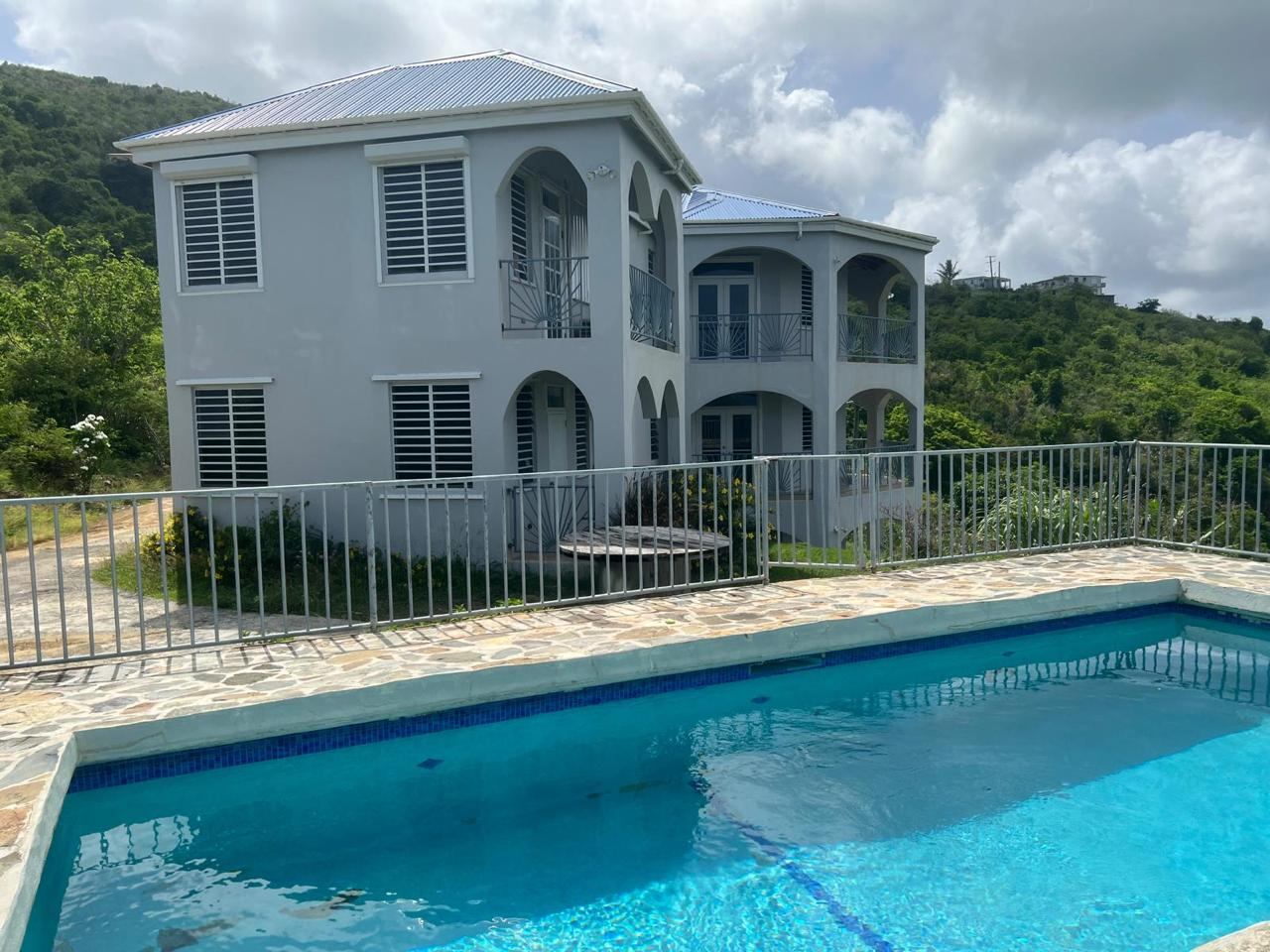 Two-story gray house with a blue roof and a blue swimming pool in the foreground.