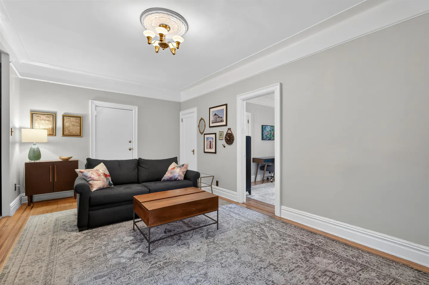 Living room with a black sofa, wooden coffee table, gray patterned rug, and light gray walls with framed wall art.
