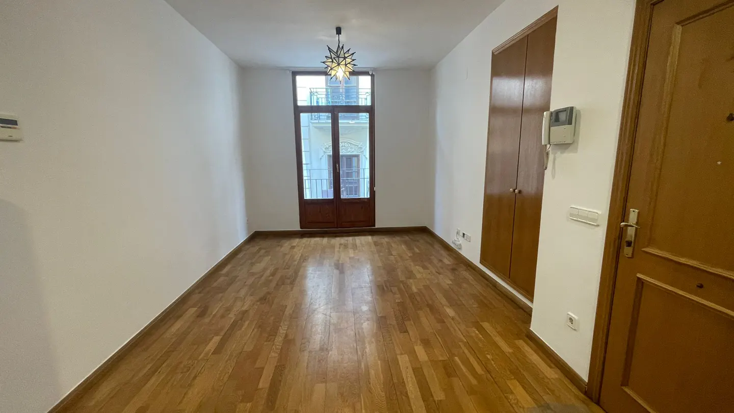 Empty room with wood floors, white walls, and a balcony door. A star-shaped light fixture hangs from the ceiling.