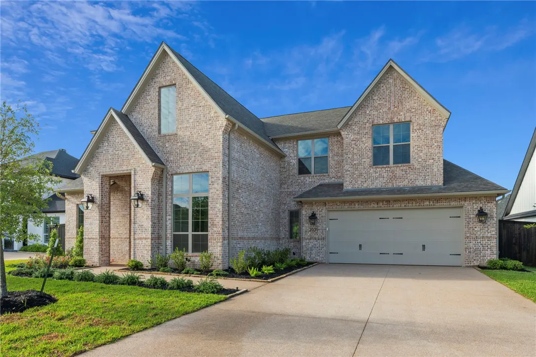 Two-story brick house with a gray roof, a two-car garage, and a well-manicured lawn under a blue sky.