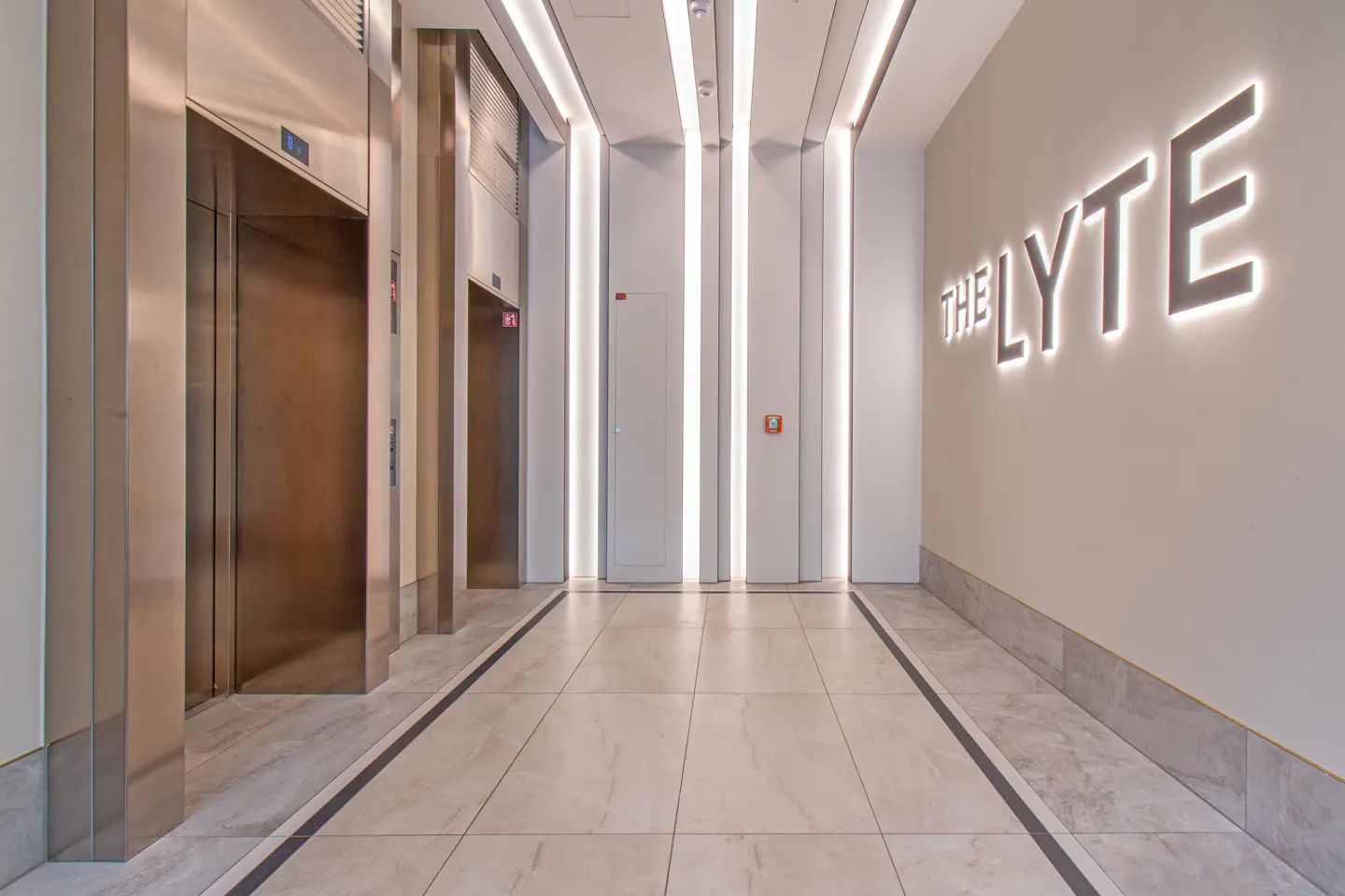 Modern lobby with marble floors, stainless steel elevators, and "THE LYTE" signage on a white wall.