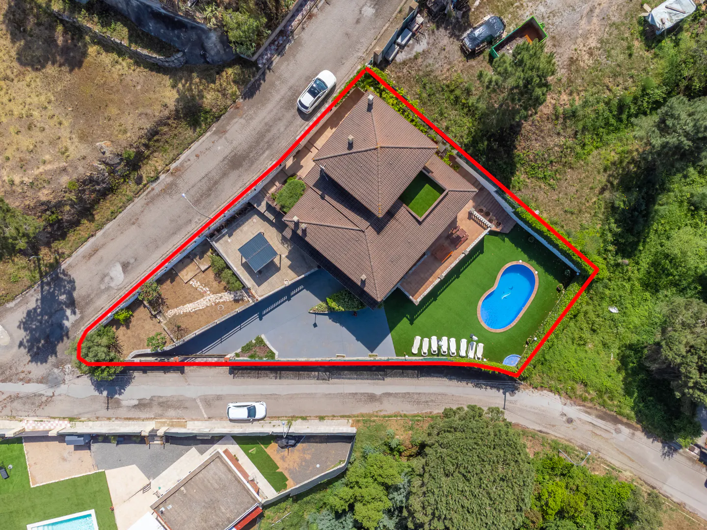 Aerial view of a brown-roofed house with a pool, lawn chairs, and a red property line.