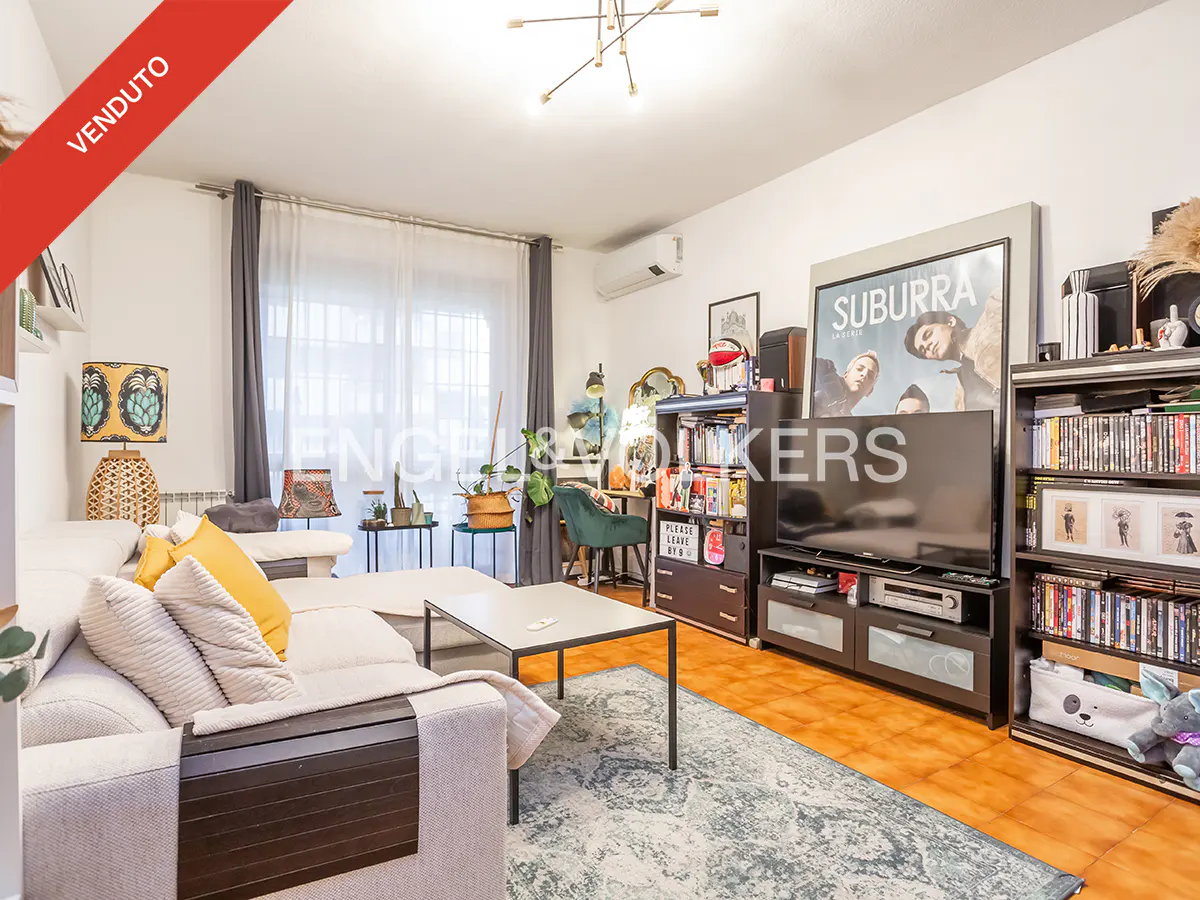 Bright living room with a white sofa, yellow pillows, a coffee table, and a TV with shelves. "VENDUTO" banner in the corner.