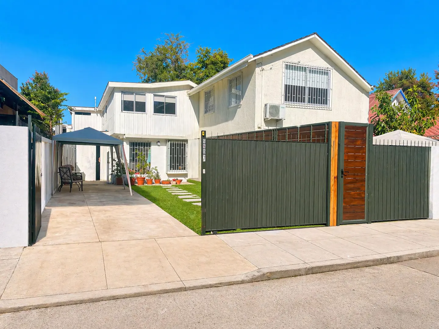 Two-story white house with a dark green fence, a concrete driveway, and a blue sky.