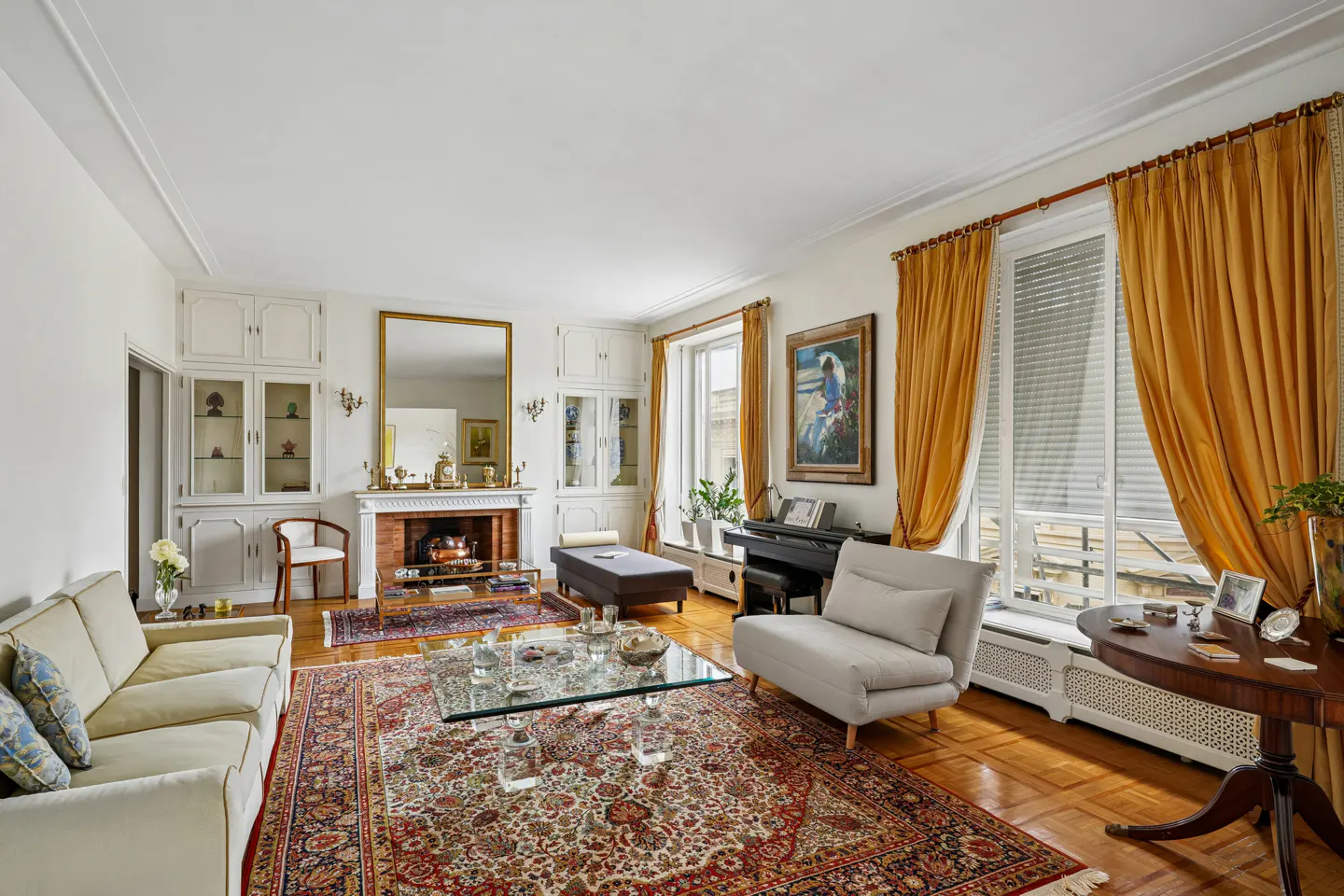 Elegant living room with a beige sofa, glass coffee table, fireplace, piano, and vibrant gold curtains on hardwood floors.