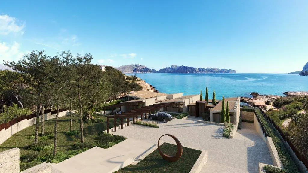 Luxury beachfront property with a car parked in the driveway, overlooking the turquoise ocean and distant mountains.