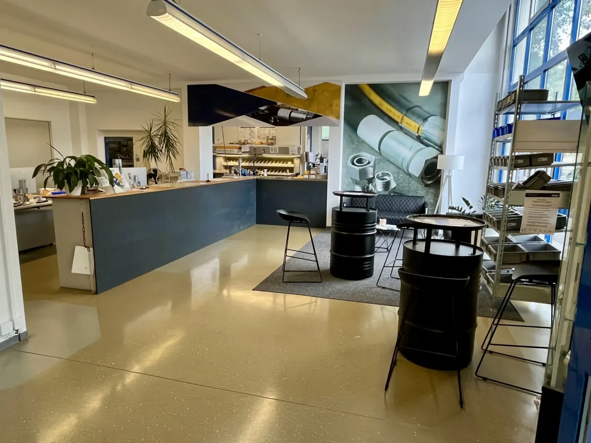 Office space with a blue counter, black barrel tables, and a mural of industrial parts.