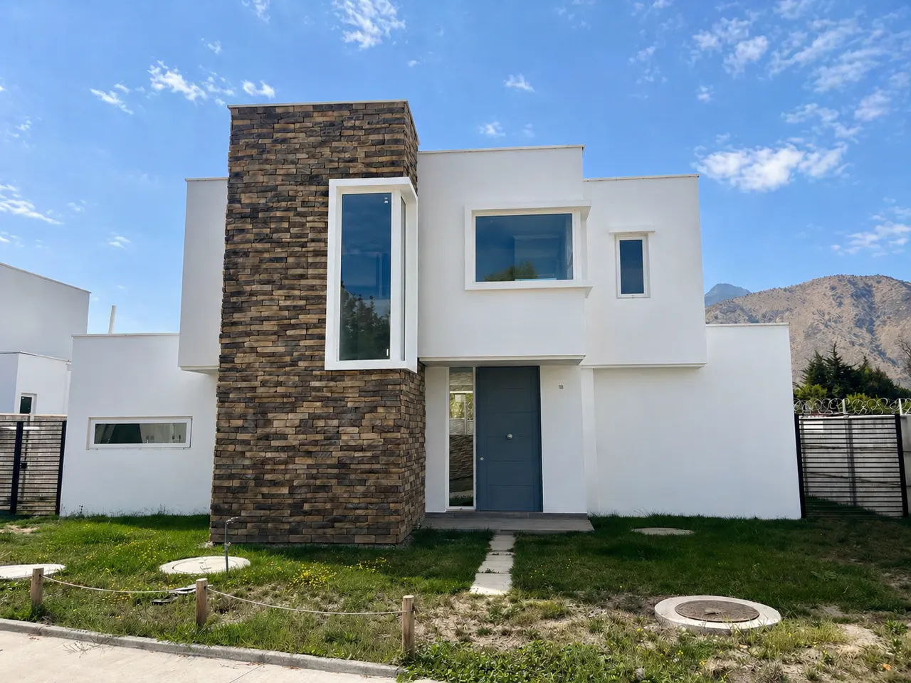 Two-story modern home with white walls, stone accent, gray door, and green lawn under a blue sky.