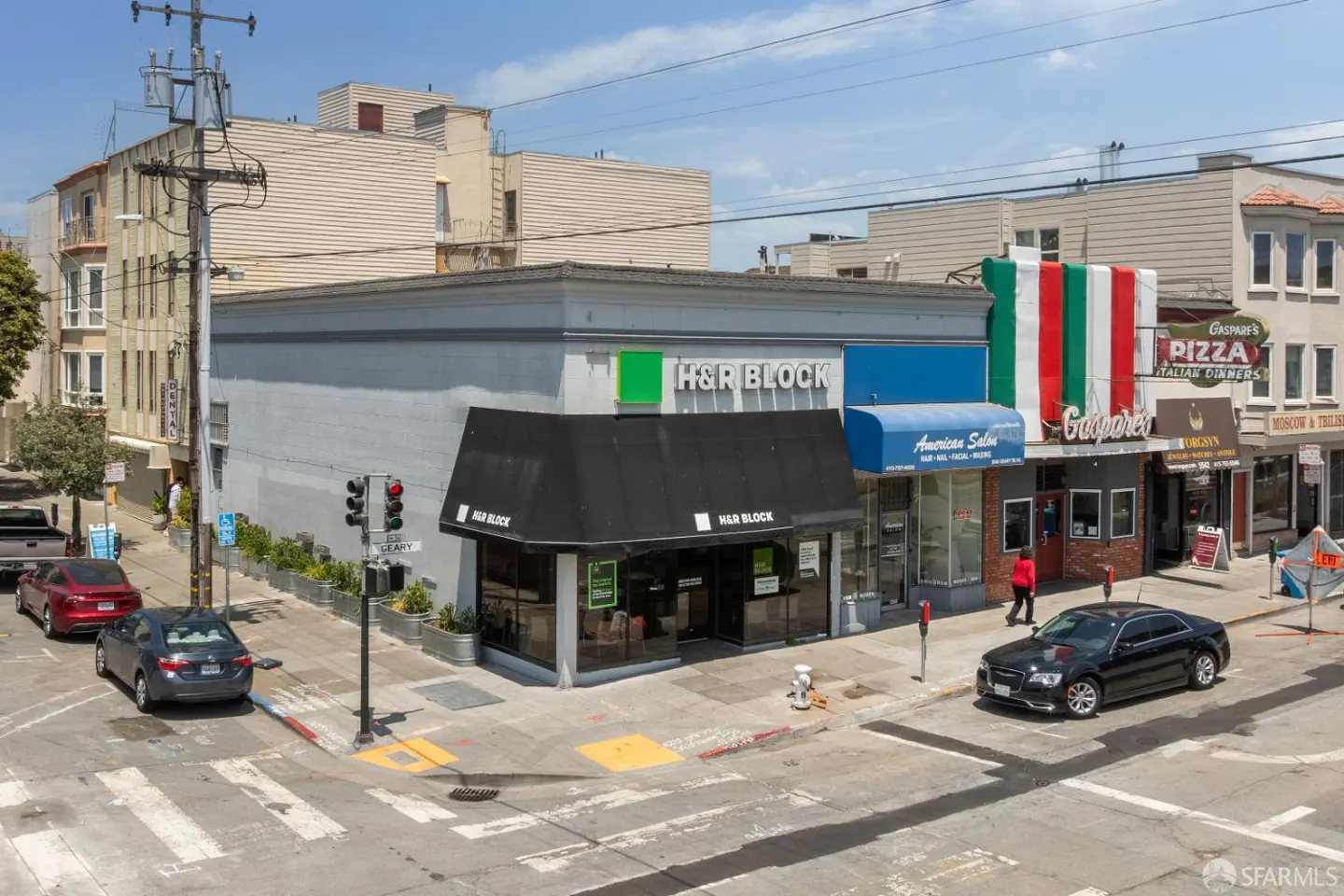 Street view of H&R Block and other businesses on a sunny day. Cars are parked and driving on the street.