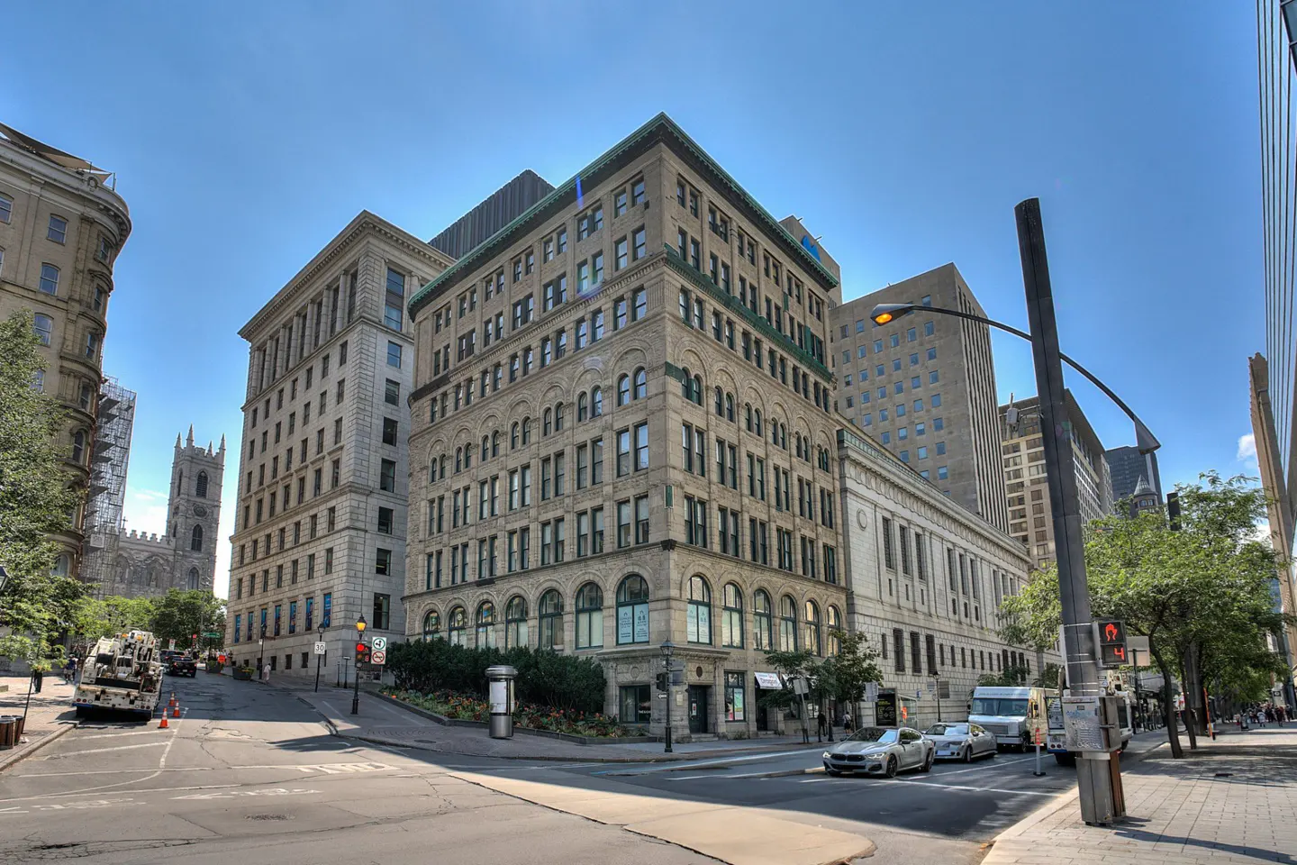 Cityscape view of Montreal, Canada, featuring historic stone buildings, a church tower, and street traffic under a blue sky.