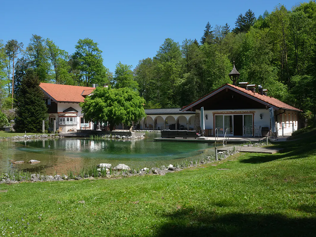 Estate view of a pond with two houses, one with a red roof, and green trees in the background.