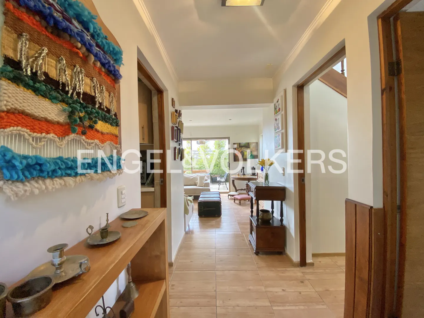 Hallway view with wood floors, white walls, and open floor plan. A colorful tapestry hangs on the left wall.