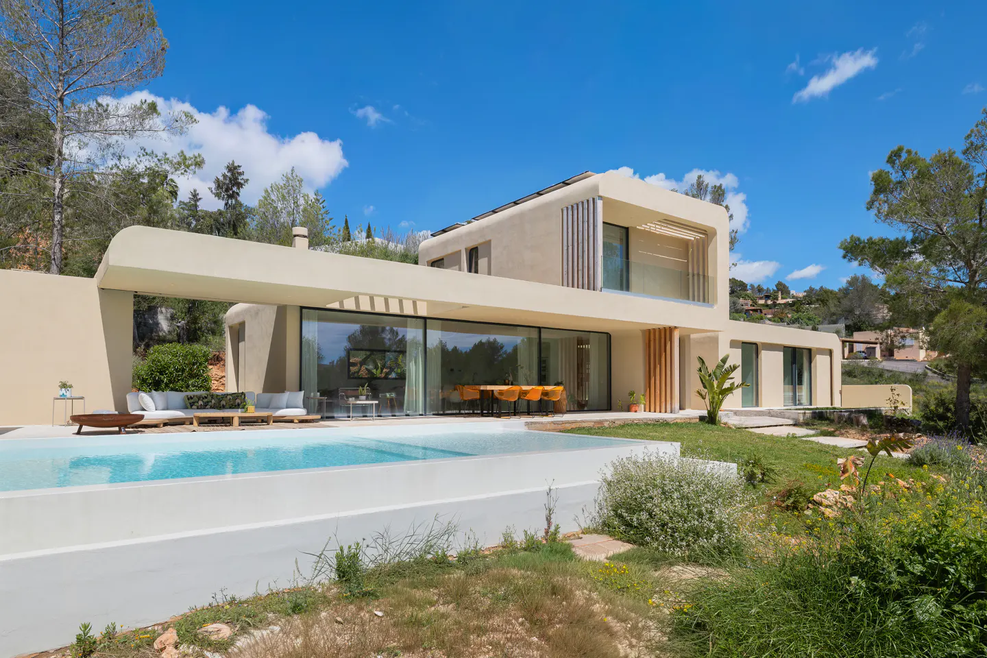 Modern beige house with a pool. Large glass windows reflect the trees. Blue sky with clouds.