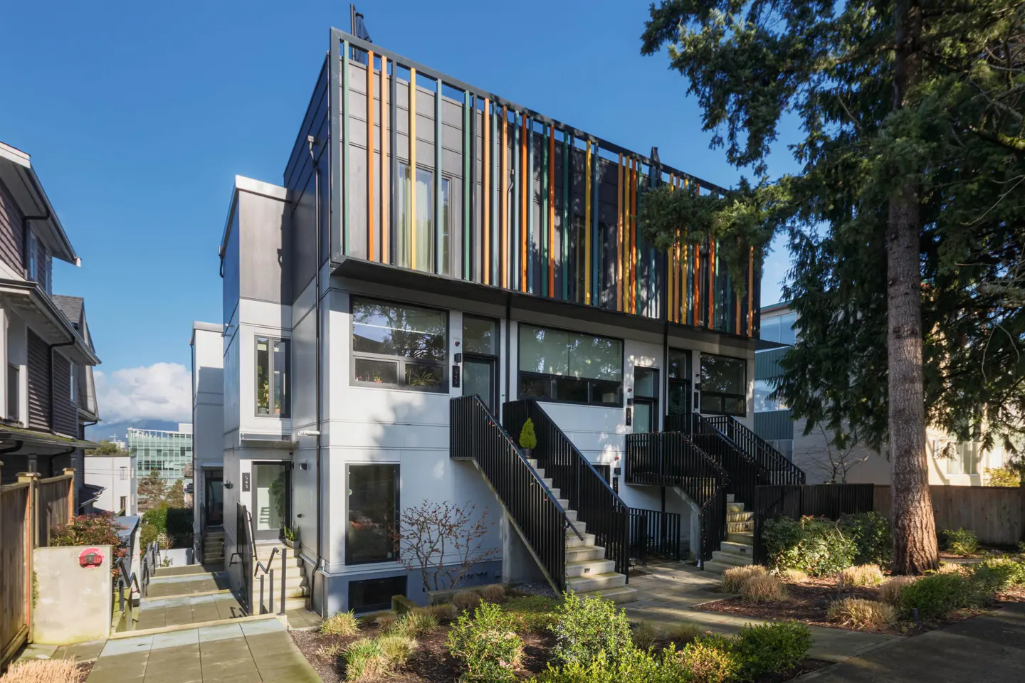Modern townhouses with gray and white exteriors, black stairs, and colorful vertical slats on the upper level.