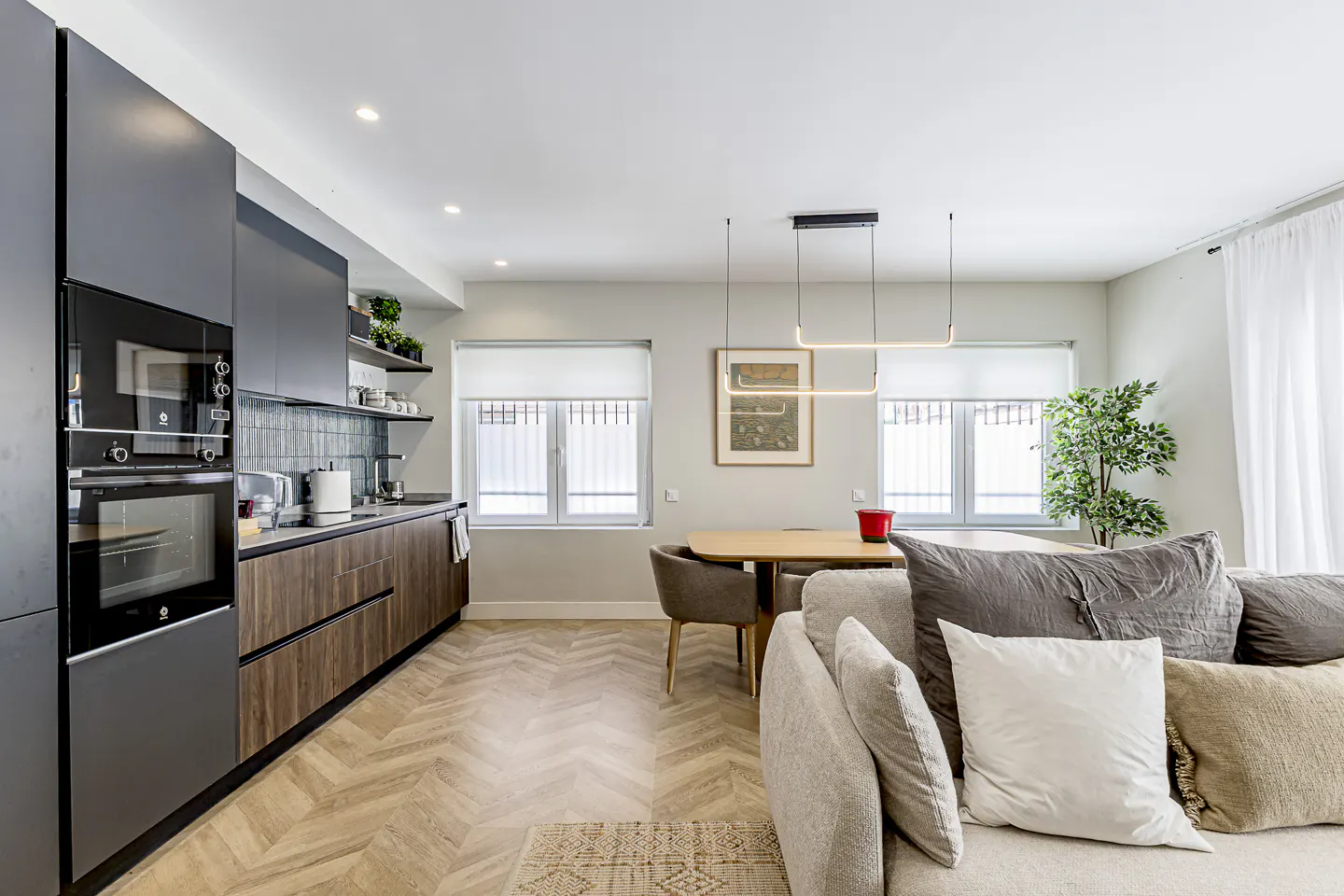 Open-concept living space with gray cabinets, wood accents, herringbone floors, dining table, and a comfortable sofa.