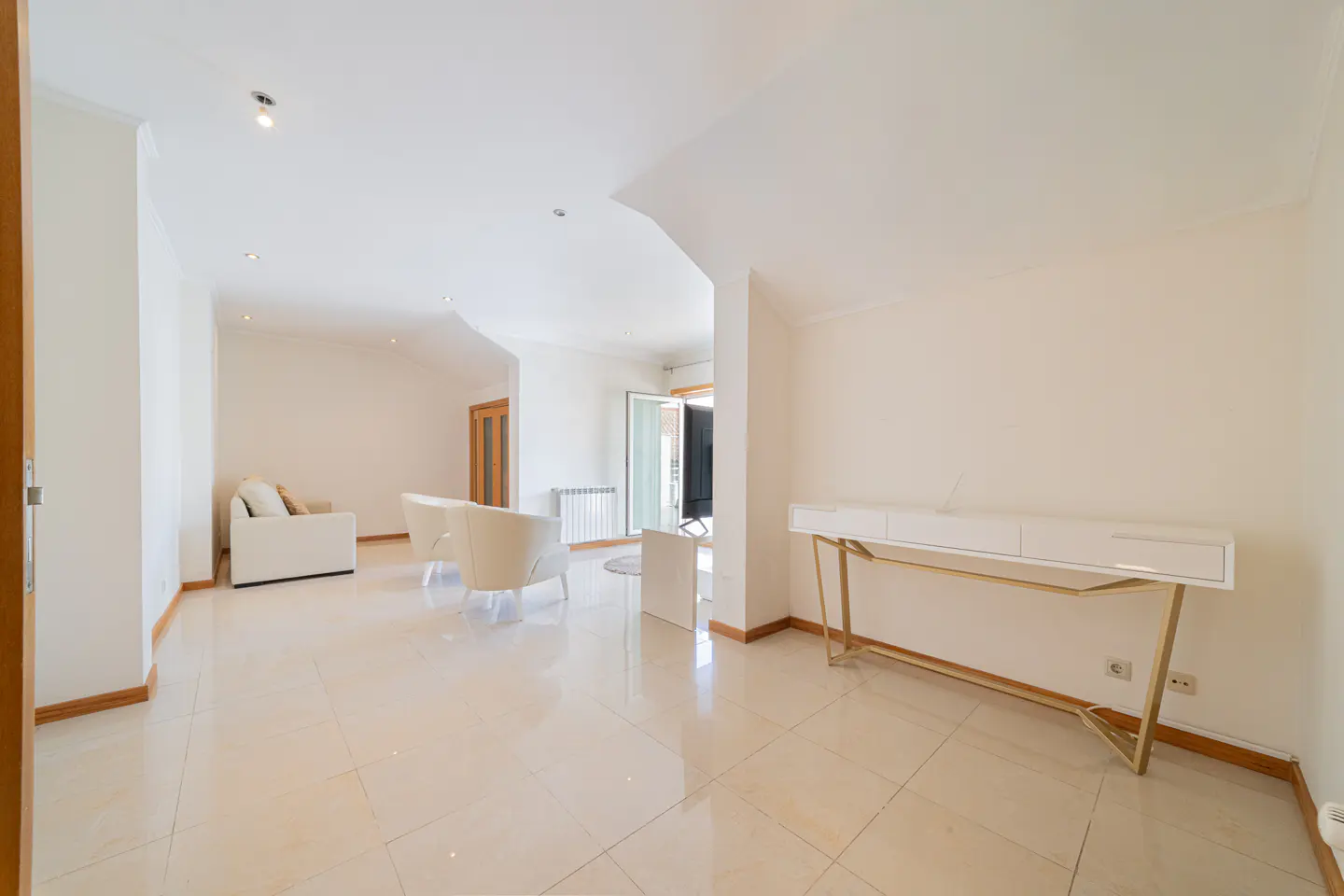 Bright, modern living room with white walls, tile floors, and minimalist furniture. A gold-legged console table stands against the wall.