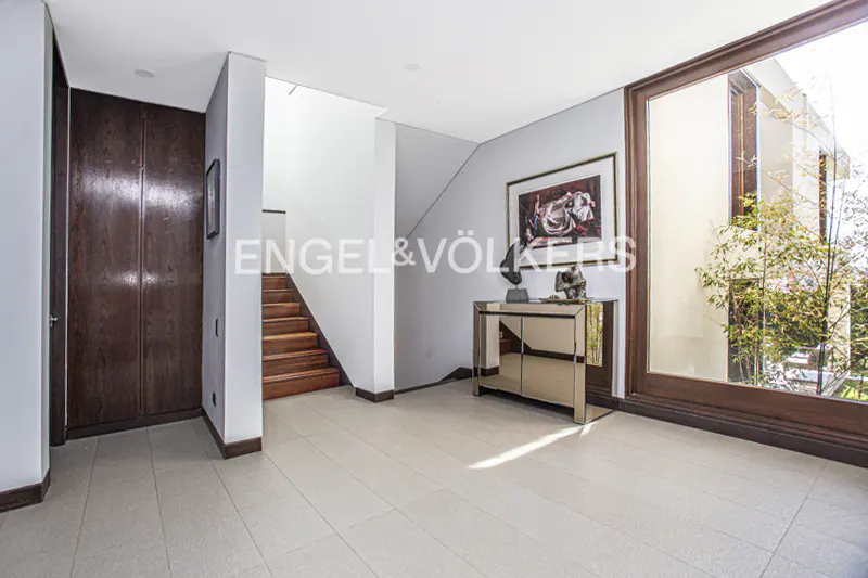Foyer with wood stairs, closet, and large window. A mirrored console table sits below a framed painting. The floor is tiled in light gray.