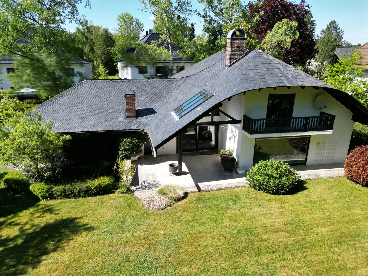Aerial view of a modern white house with a dark gray roof, chimney, balcony, and green lawn.