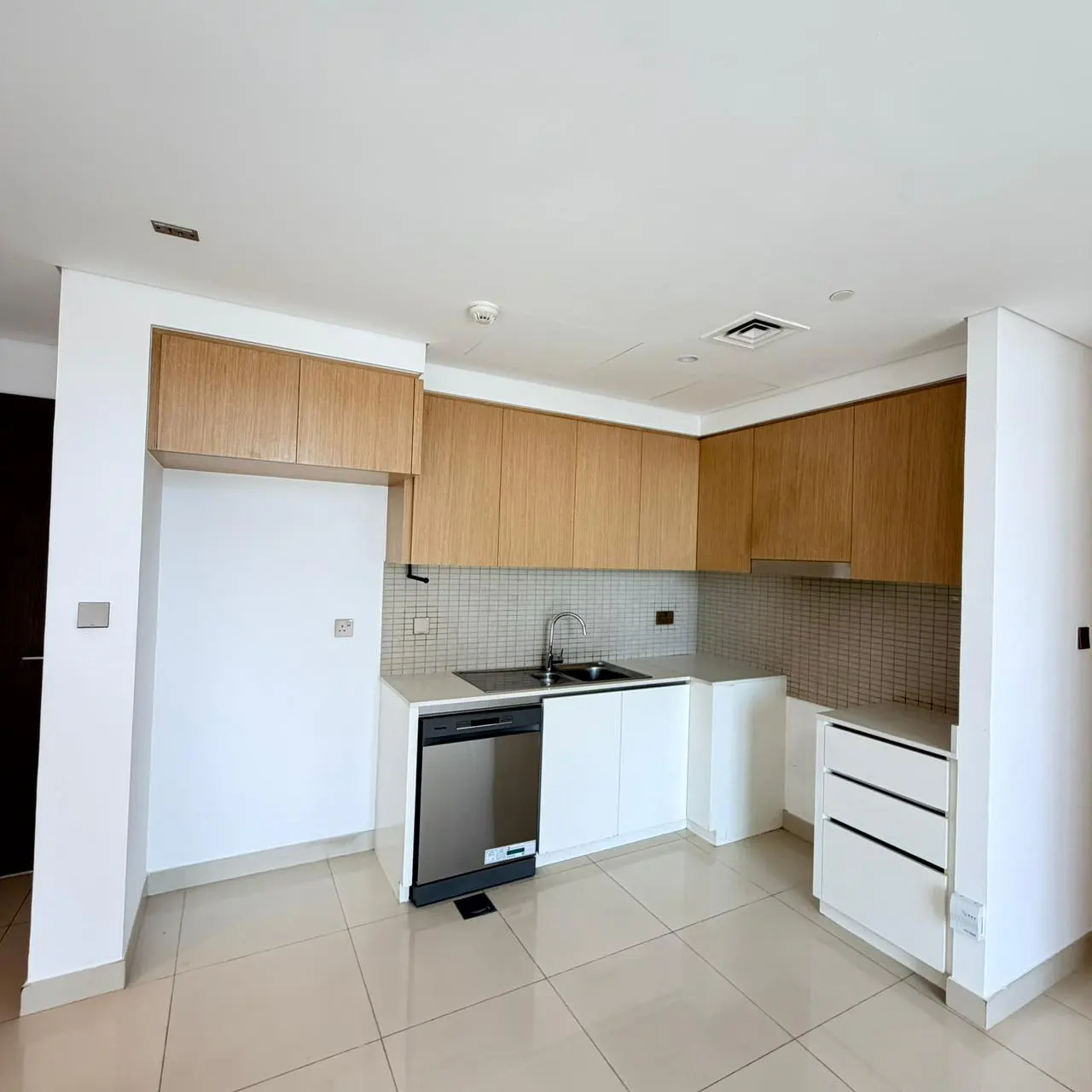 A bright, modern kitchen with light wood cabinets, white countertops, and stainless steel appliances.