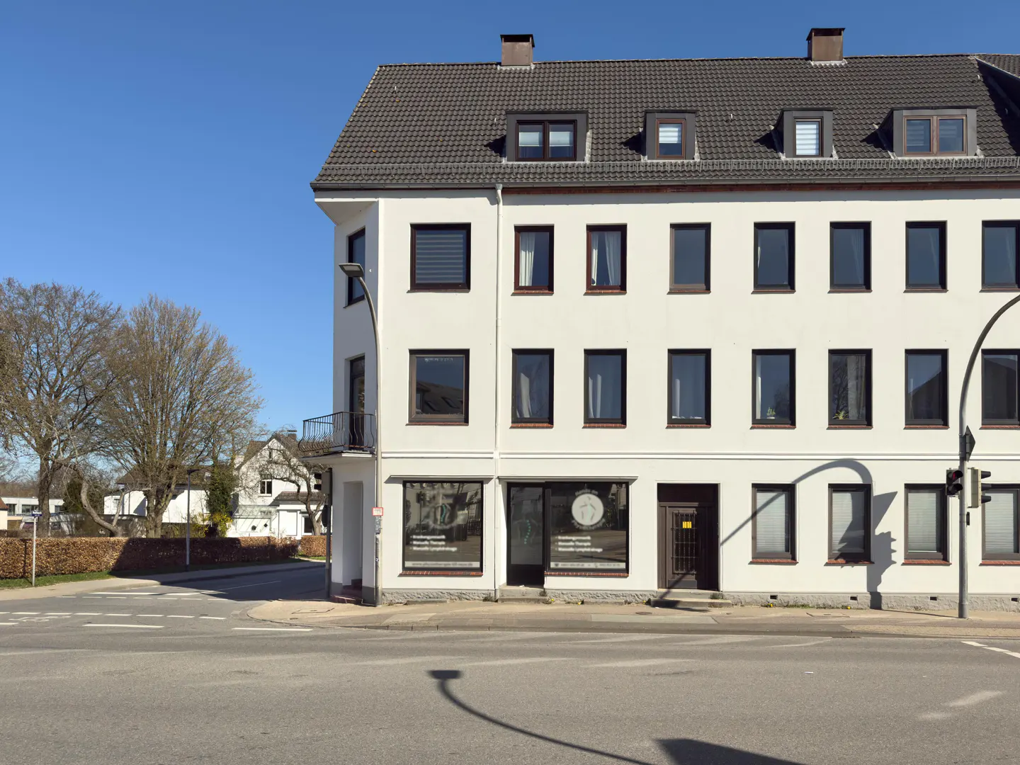 A three-story white building with a gray roof and dark windows on a sunny day.