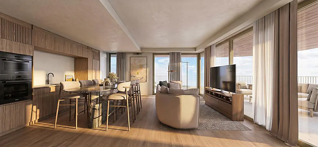 A modern apartment interior with wood floors, cabinets, and a kitchen island. Large windows offer a view of the ocean.