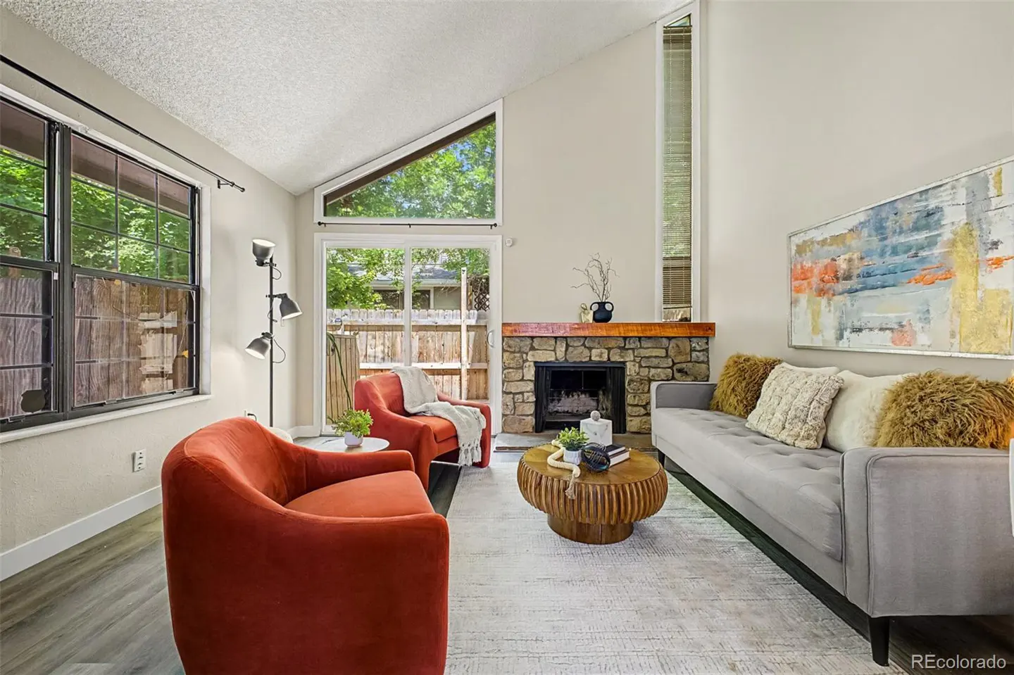 Living room with vaulted ceiling, stone fireplace, grey sofa, two orange armchairs, and a round wooden coffee table.