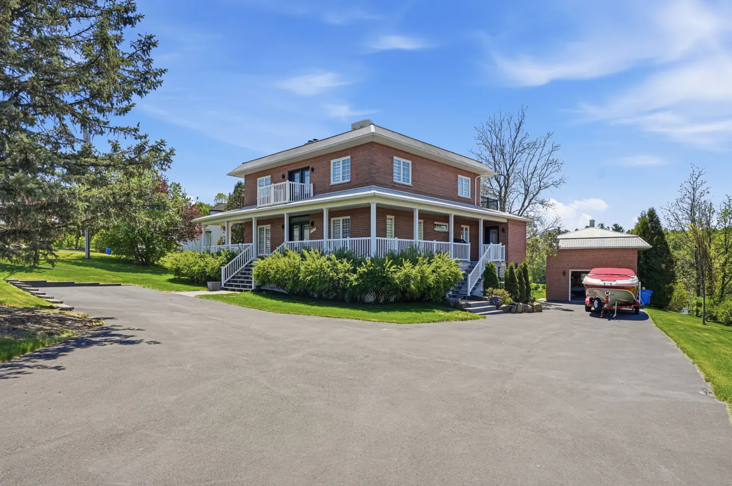 Two-story brick house with white trim, a wraparound porch, and a detached garage with a boat parked outside.