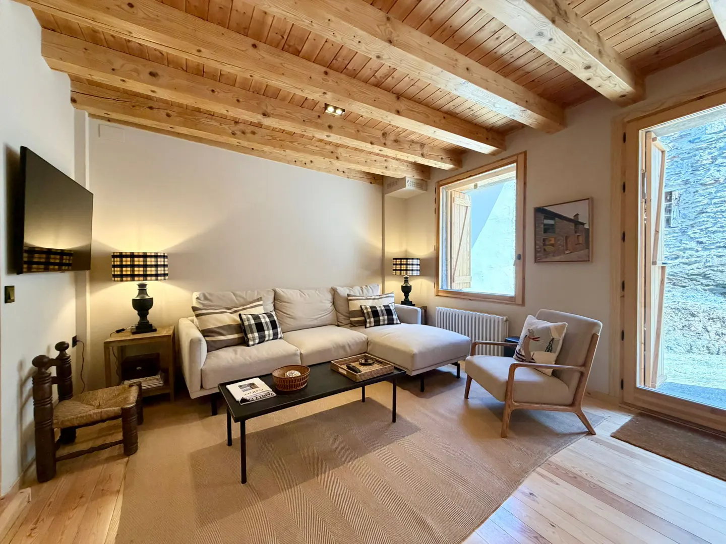 Living room with wooden ceiling, beige sofa, black coffee table, and open door to a stone wall.