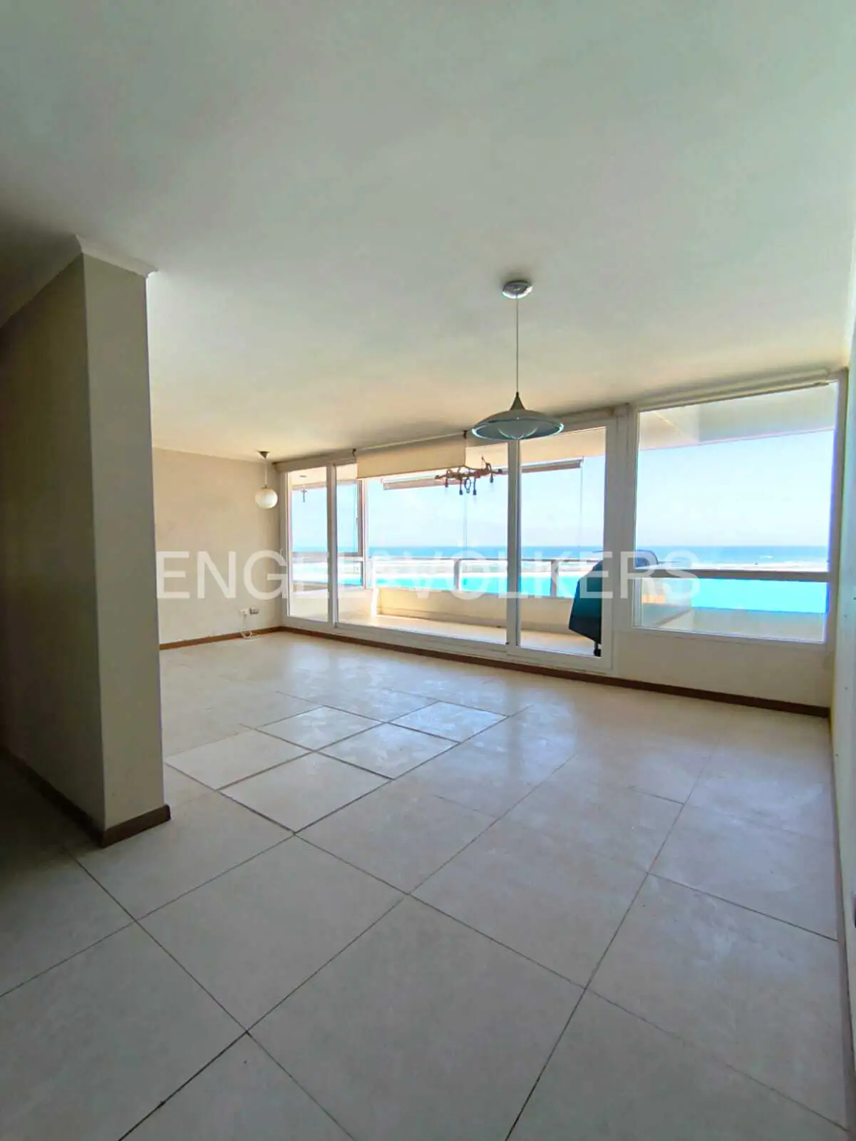 Spacious, empty living room with light tile floors, large windows, and a panoramic view of the blue ocean.