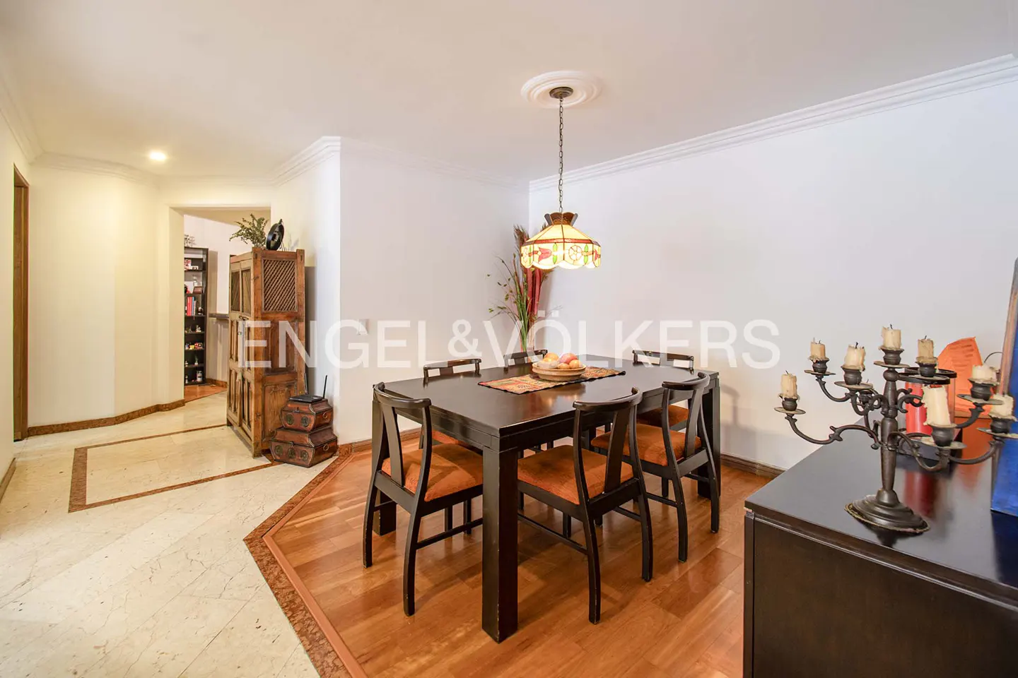 A dining room with a dark wood table and six chairs with orange cushions. A candelabra sits on a dark wood sideboard.