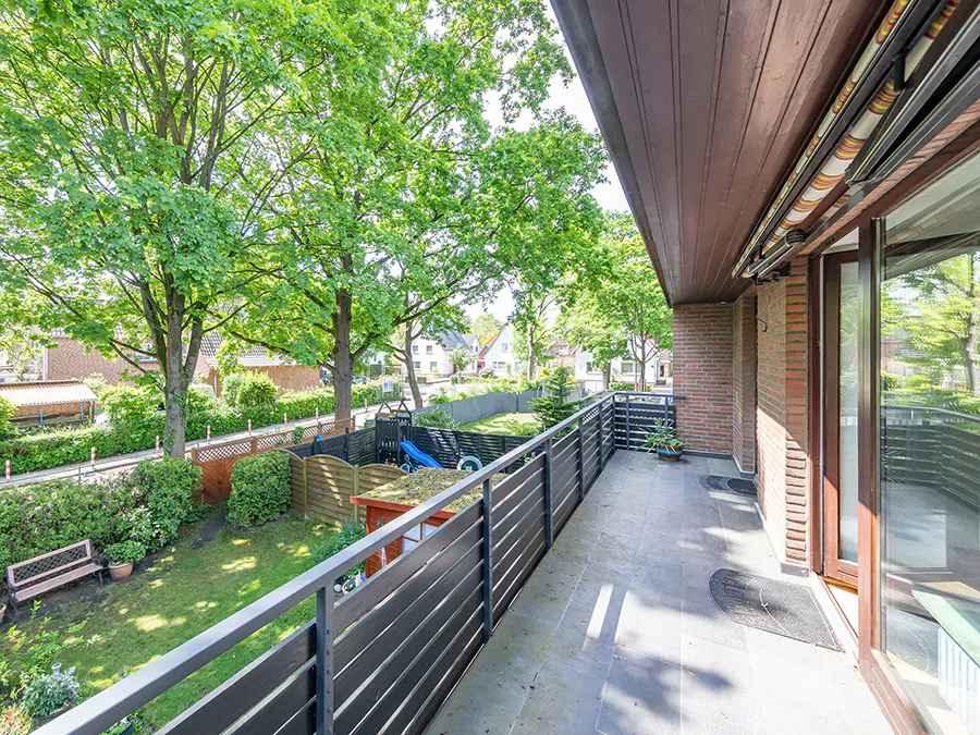 Balcony view of a green backyard with trees, a playset, and a bench. The balcony has a dark gray railing and a gray tile floor.