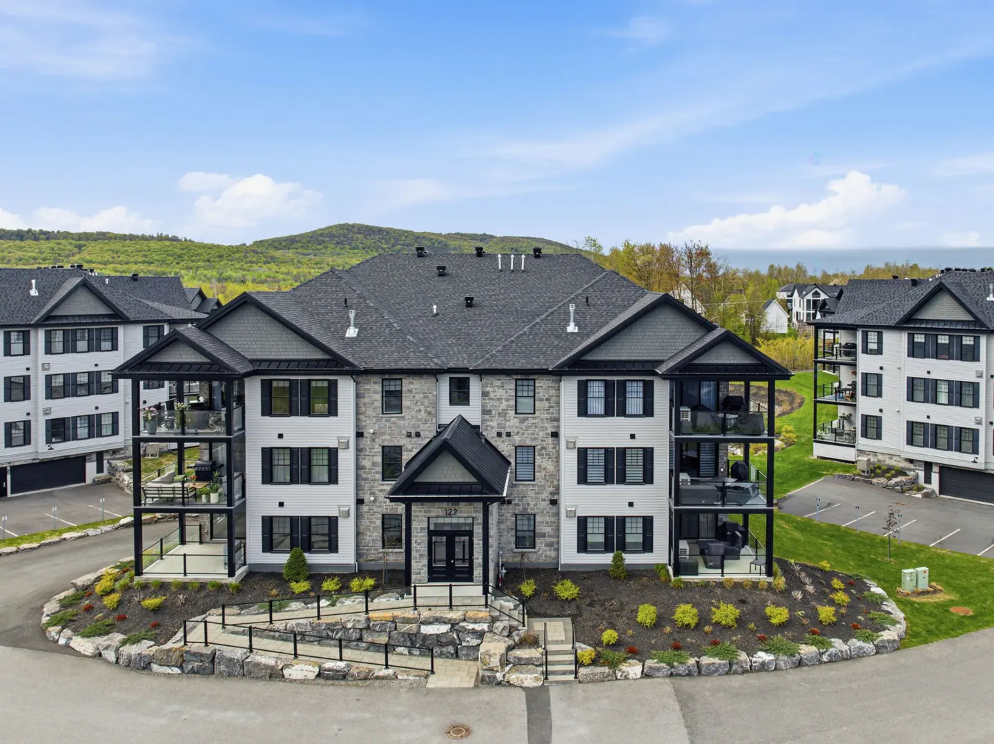 Three-story apartment building with white siding, stone accents, and black trim. Balconies are visible. Landscaped front yard.
