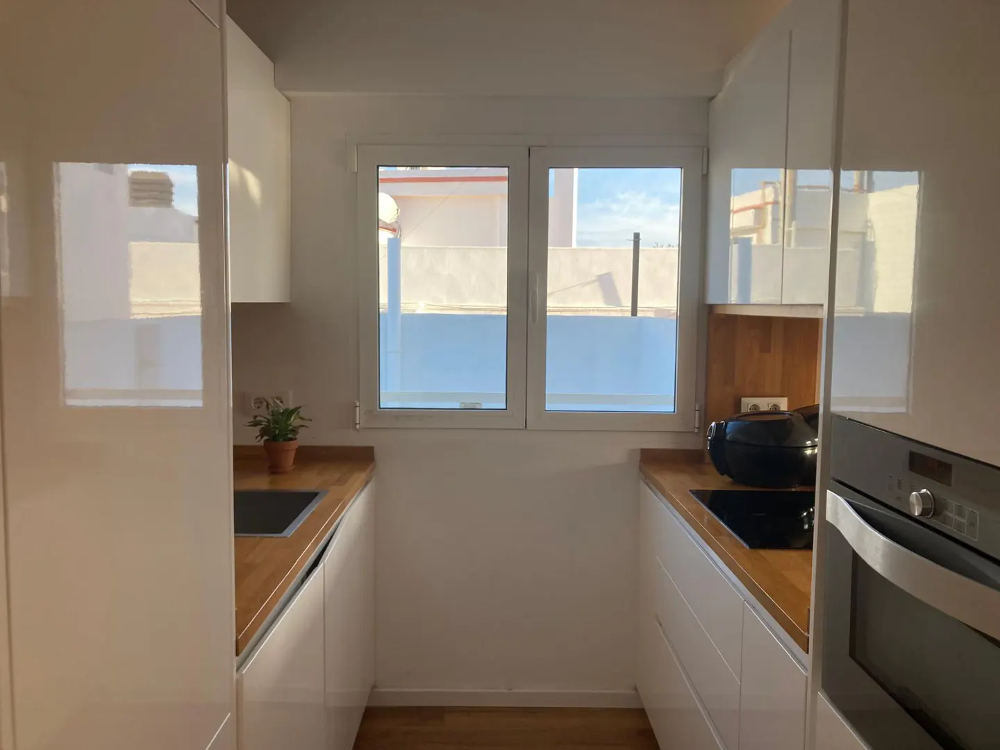 A narrow kitchen with white cabinets, wood countertops, and a window. An oven is visible on the right.