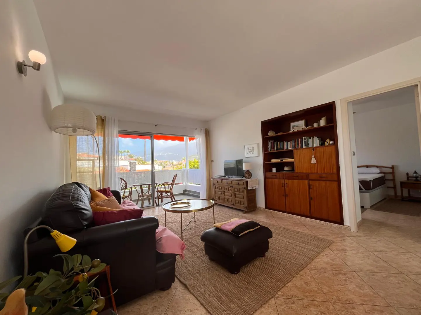 Bright living room with brown leather sofa, jute rug, and balcony with red awning overlooking a scenic view.