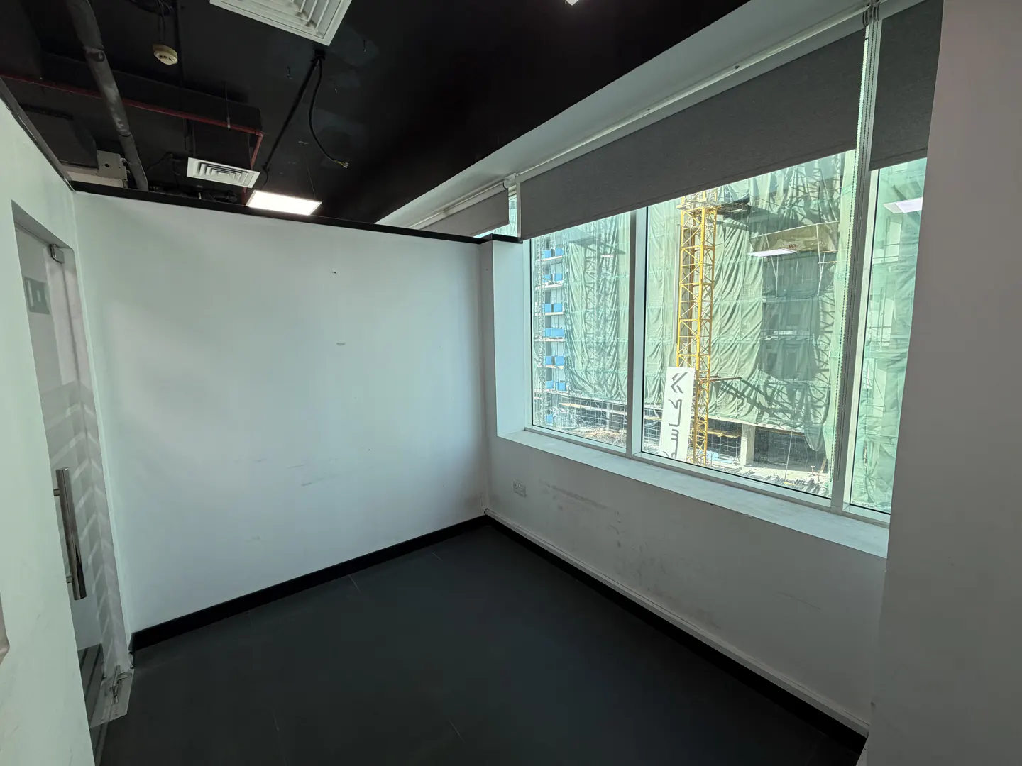 Empty office space with white walls, black floor and ceiling. Large window with construction crane view.