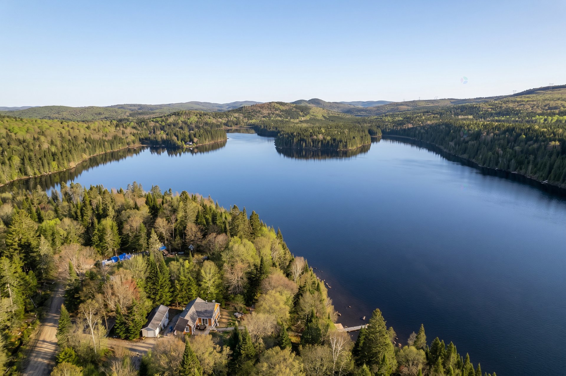 Aerial view of a lake surrounded by green forests, with a house nestled among the trees on the shoreline.
