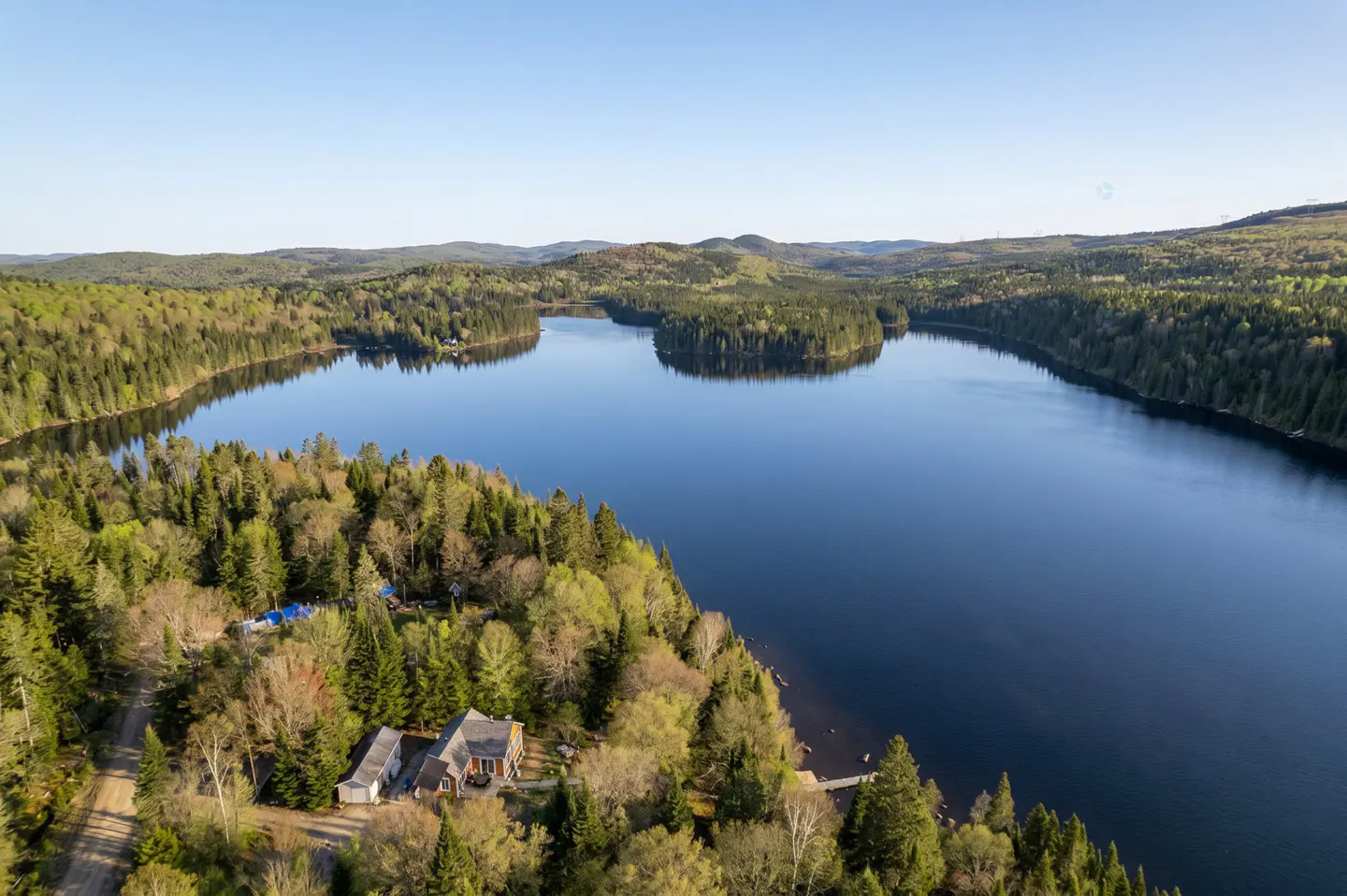 Aerial view of a lake surrounded by green forests, with a house nestled among the trees on the shoreline.