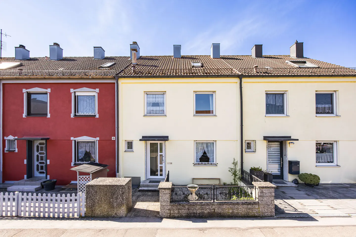 Row of three attached houses, red and yellow, with tiled roofs and chimneys under a blue sky.