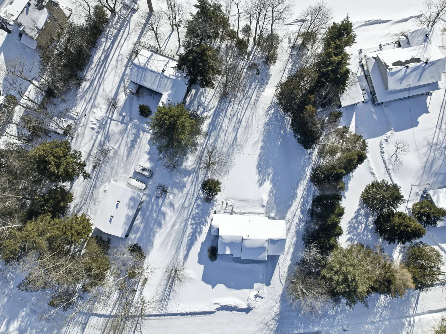 Aerial view of snow-covered houses and trees, casting long shadows on a sunny winter day.