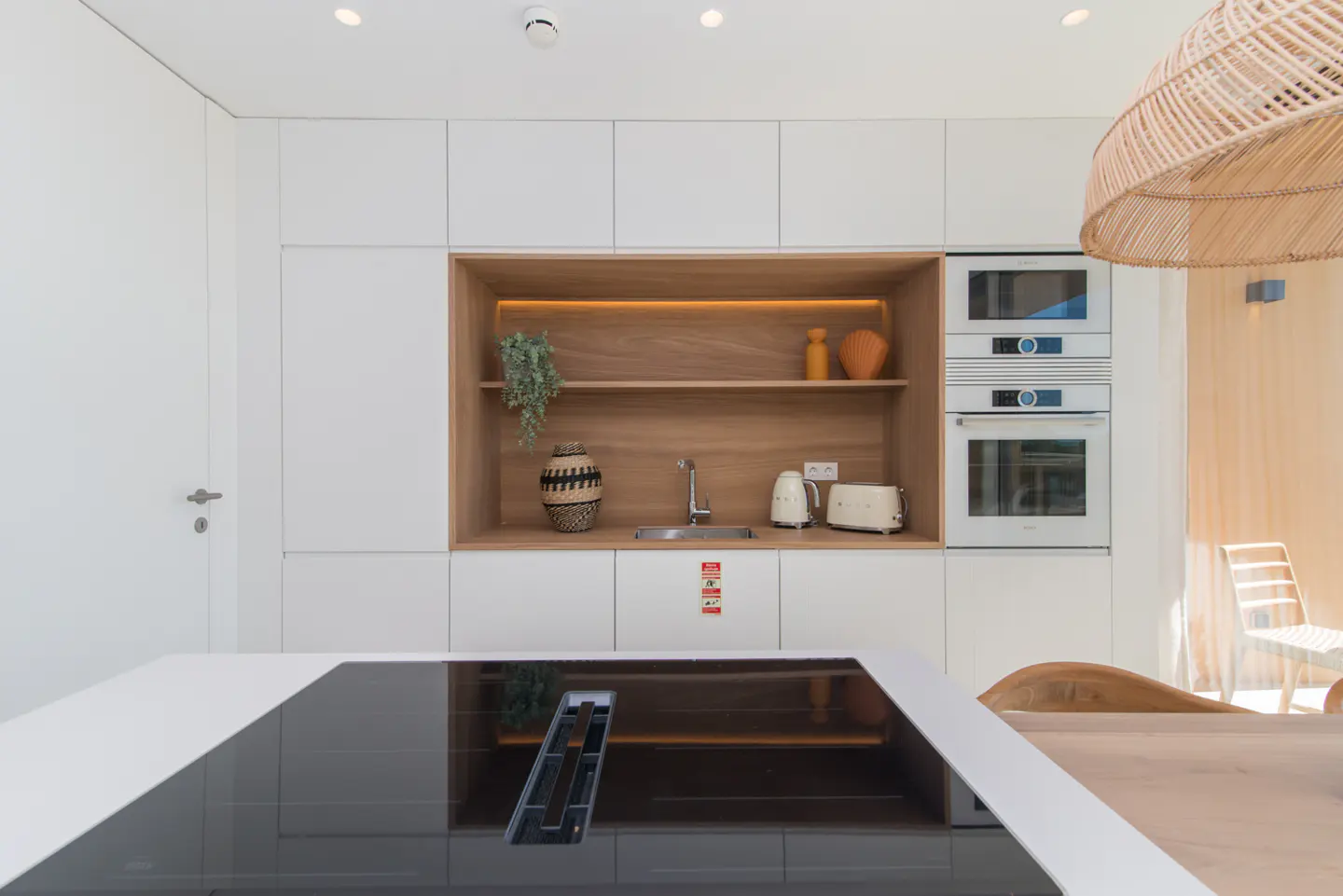 Modern kitchen with white cabinets, stainless steel sink, and built-in appliances. A wooden shelf displays decorative items.