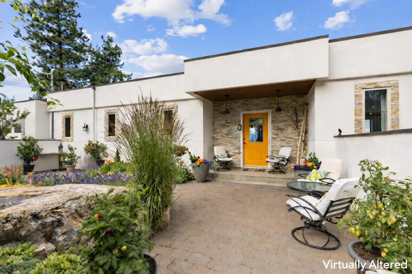Modern home exterior with a bright yellow front door, stone accent wall, patio seating, and a landscaped garden.