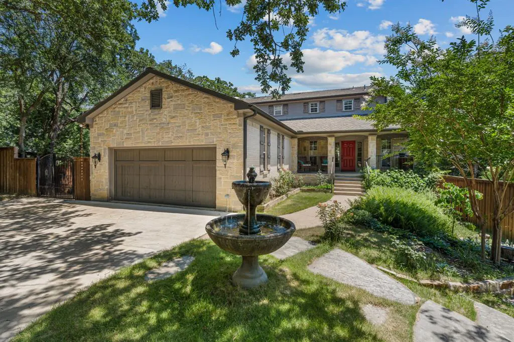 Two-story home with a stone exterior, brown garage door, red front door, and a fountain in the front yard.